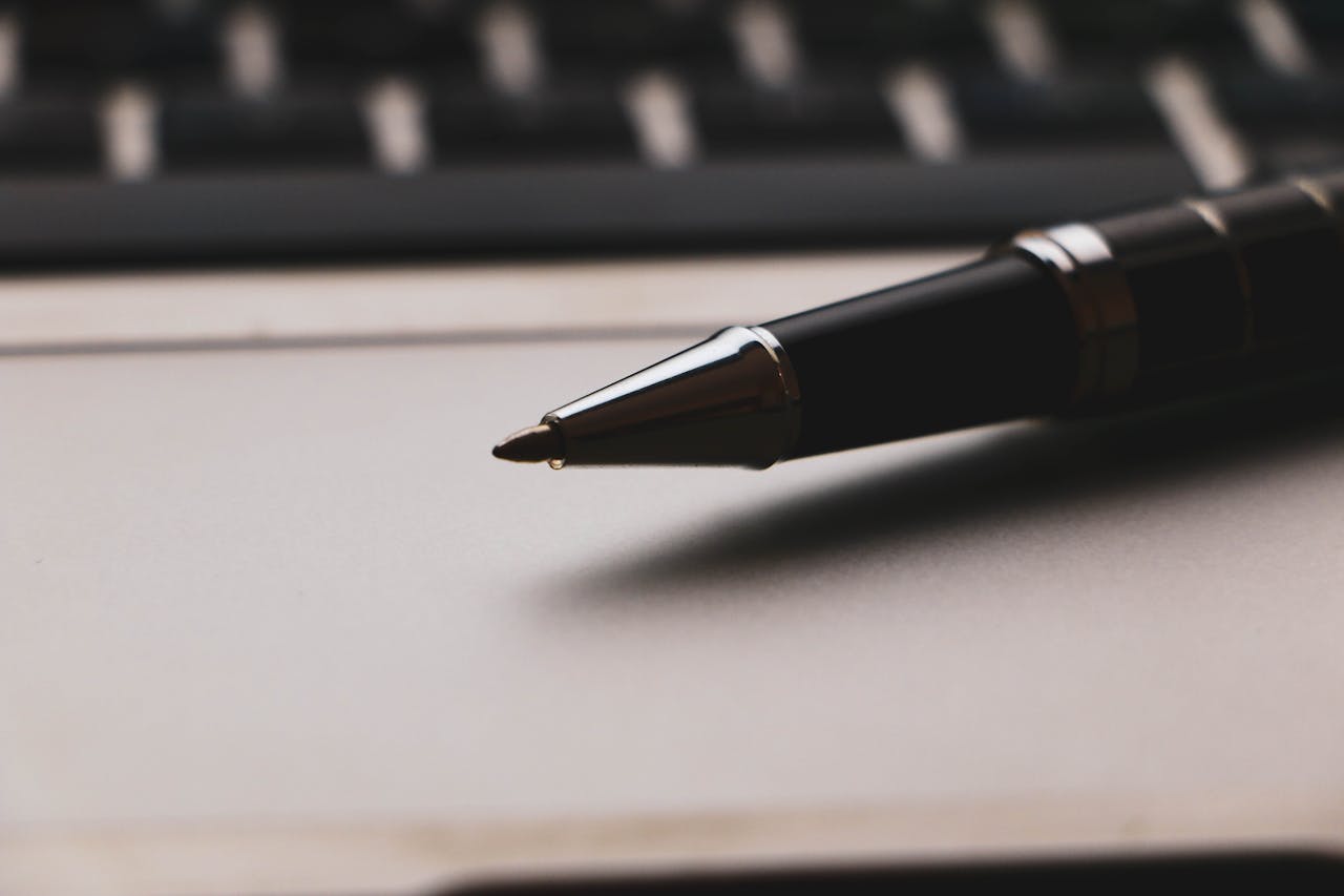 A focused close-up of a ballpoint pen resting on a laptop, emphasizing productivity.